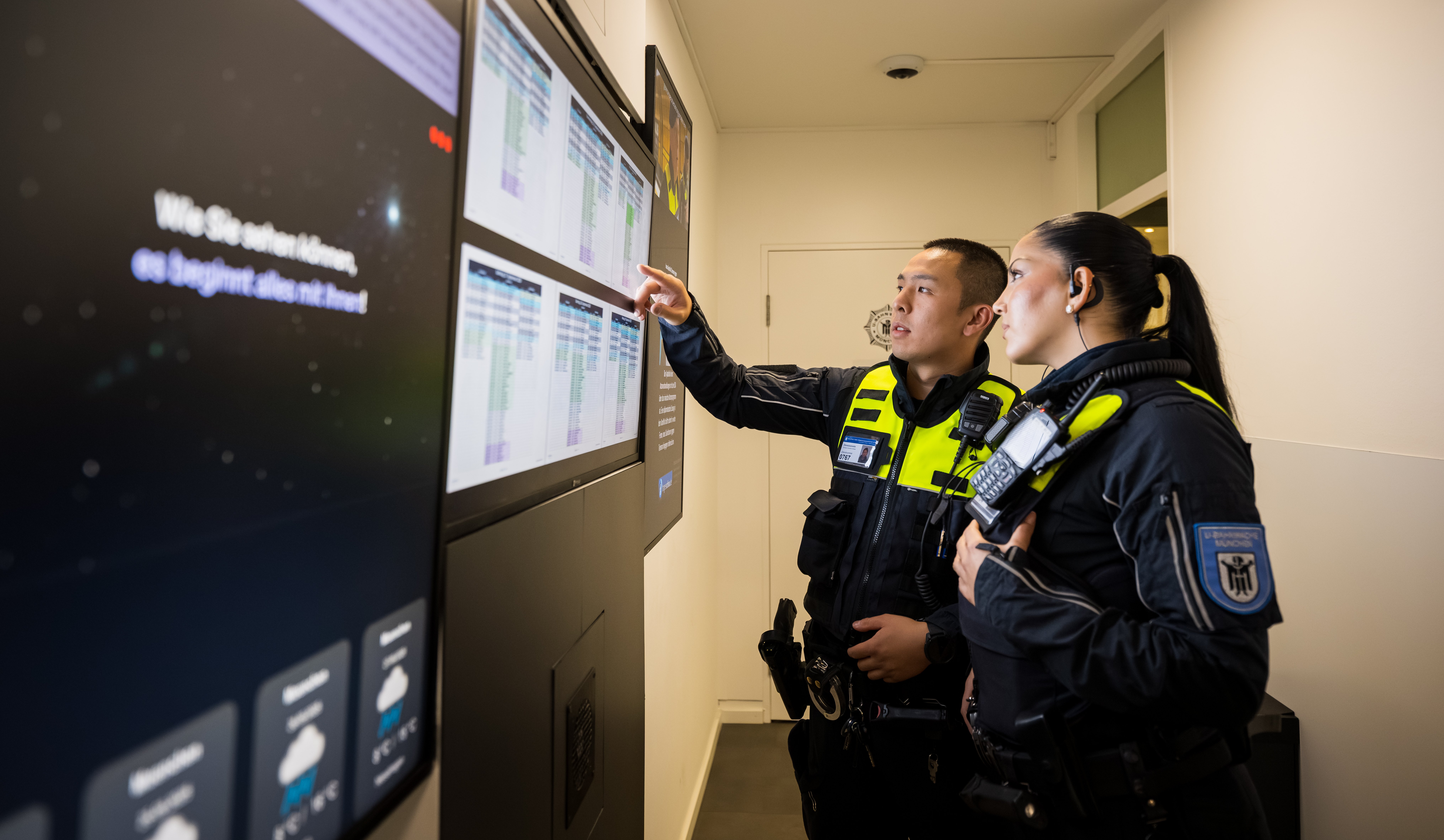 A female and a male M&uuml;nchner U-Bahnwache guard looking at data from Securitas on big screens.